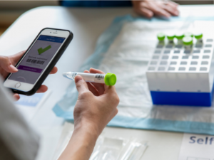 Photo of a Duke student is using a cellphone app to scan a vial of saline solution provided in the COVID self-testing kit.